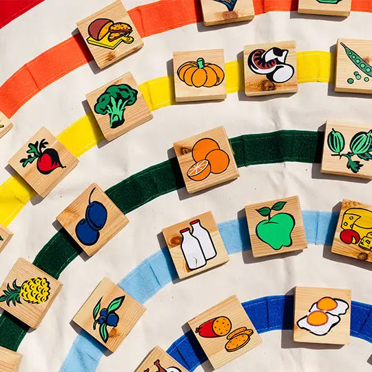 Ein buntes Ernährungsspiel mit Holzplättchen, die verschiedene Lebensmittel wie Obst, Gemüse und Milchprodukte zeigen.