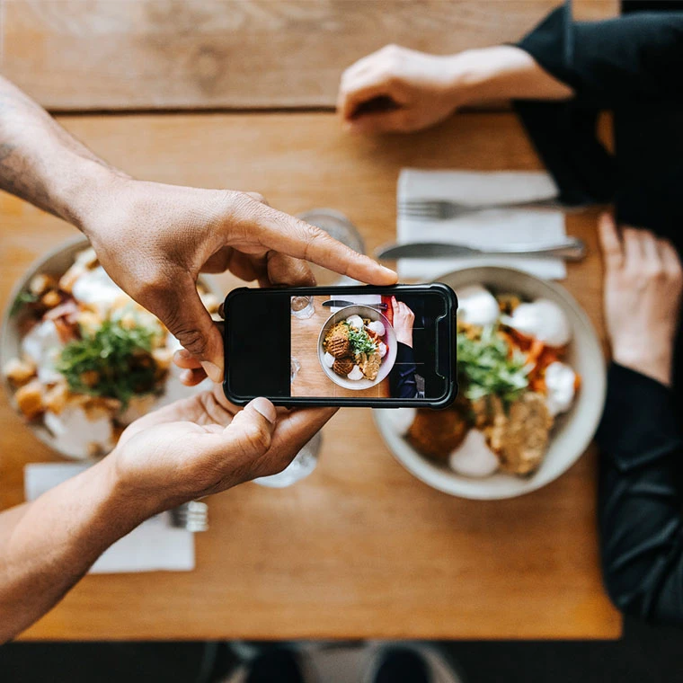 Hands photographing a dish with a smartphone.