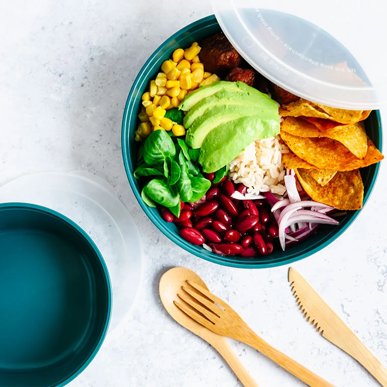 Eine bunte Bowl gefüllt mit Mais, Avocado, Bohnen, Reis, Salat und Tortilla-Chips in einer Recup-Box.