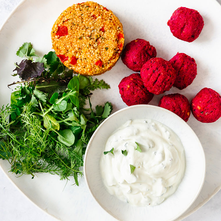 Ein Teller mit pinken Falafel-Bällchen, grünem Salat und einer Schüssel Joghurt-Dip.